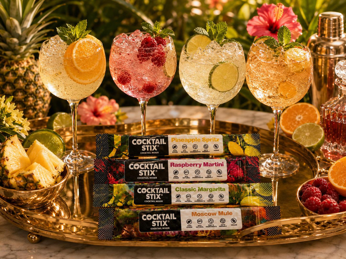 Cocktail Stix packets beside two polished drinks—one cocktail and one mocktail—on an upscale home bar or kitchen island.